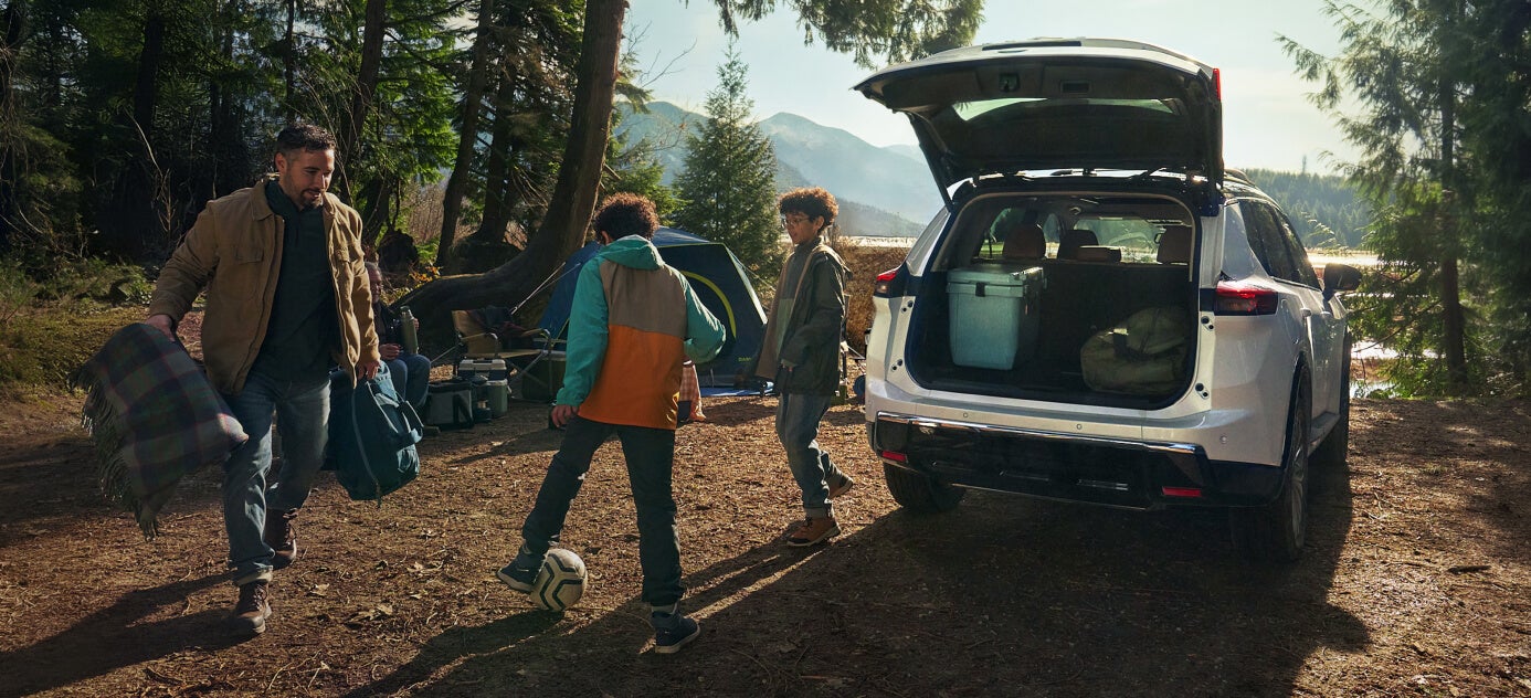Rear view of a Nissan Rogue Platinum in White Pearl with an open liftgate at a forest campsite.