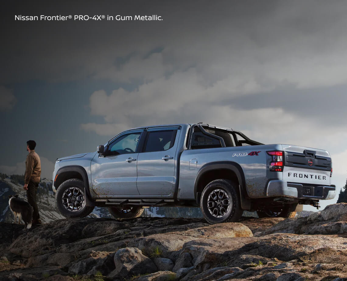 Rear three-quarter perspective of a Nissan Frontier PRO-4X in Gun Metallic parked on a rocky mountain ledge.
