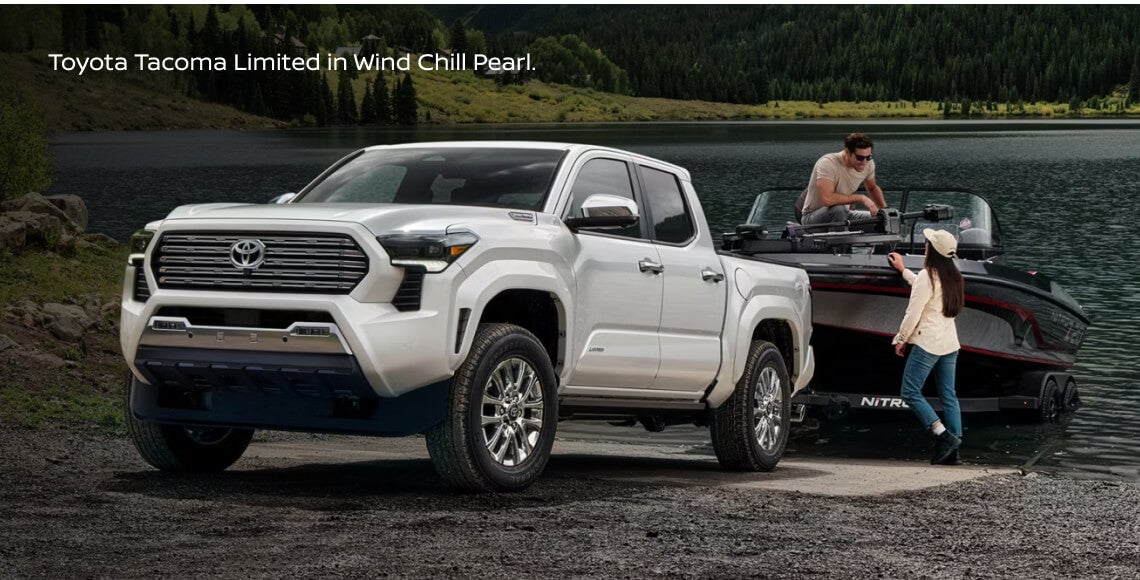 Front three-quarter view of a Toyota Tacoma Limited in Wind Chill Pearl on a boat ramp into a scenic lake.