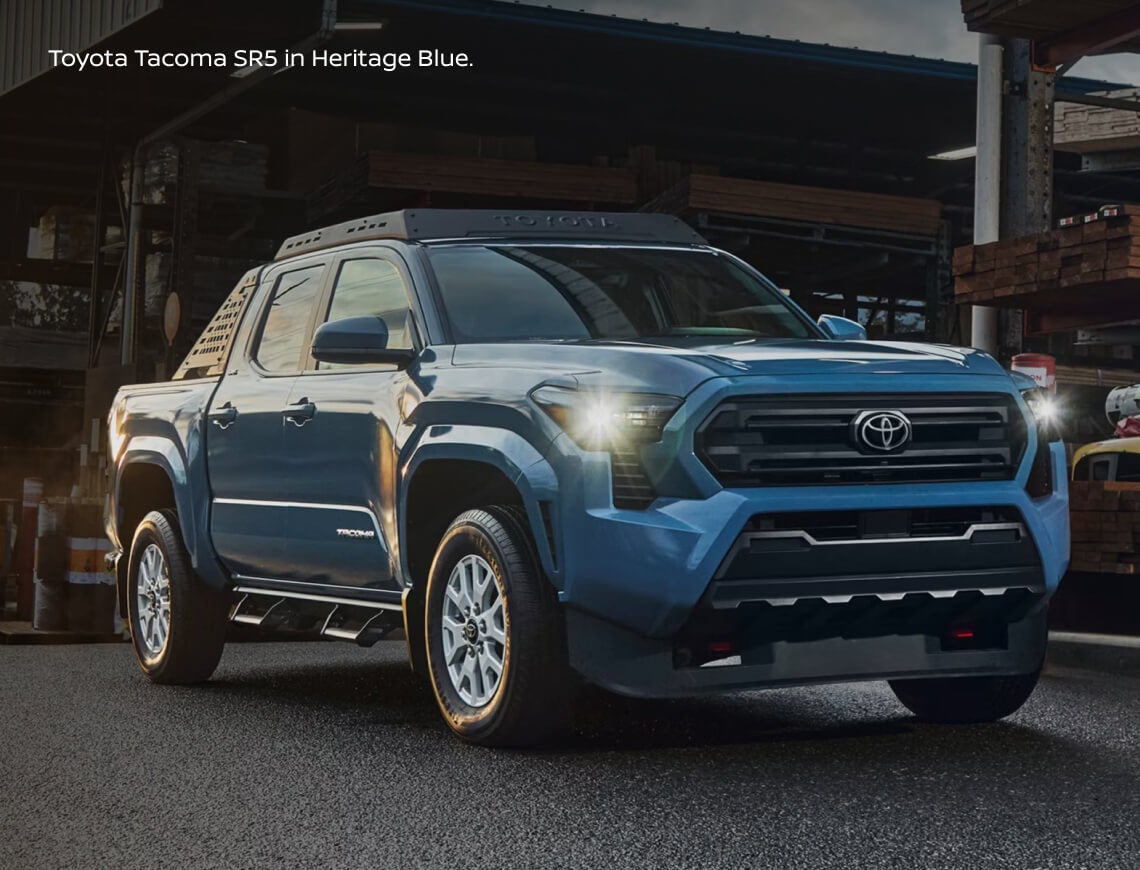 Front three-quarter view of a Toyota Tacoma SR5 in Heritage Blue equipped with an overland roof rack and side steps.