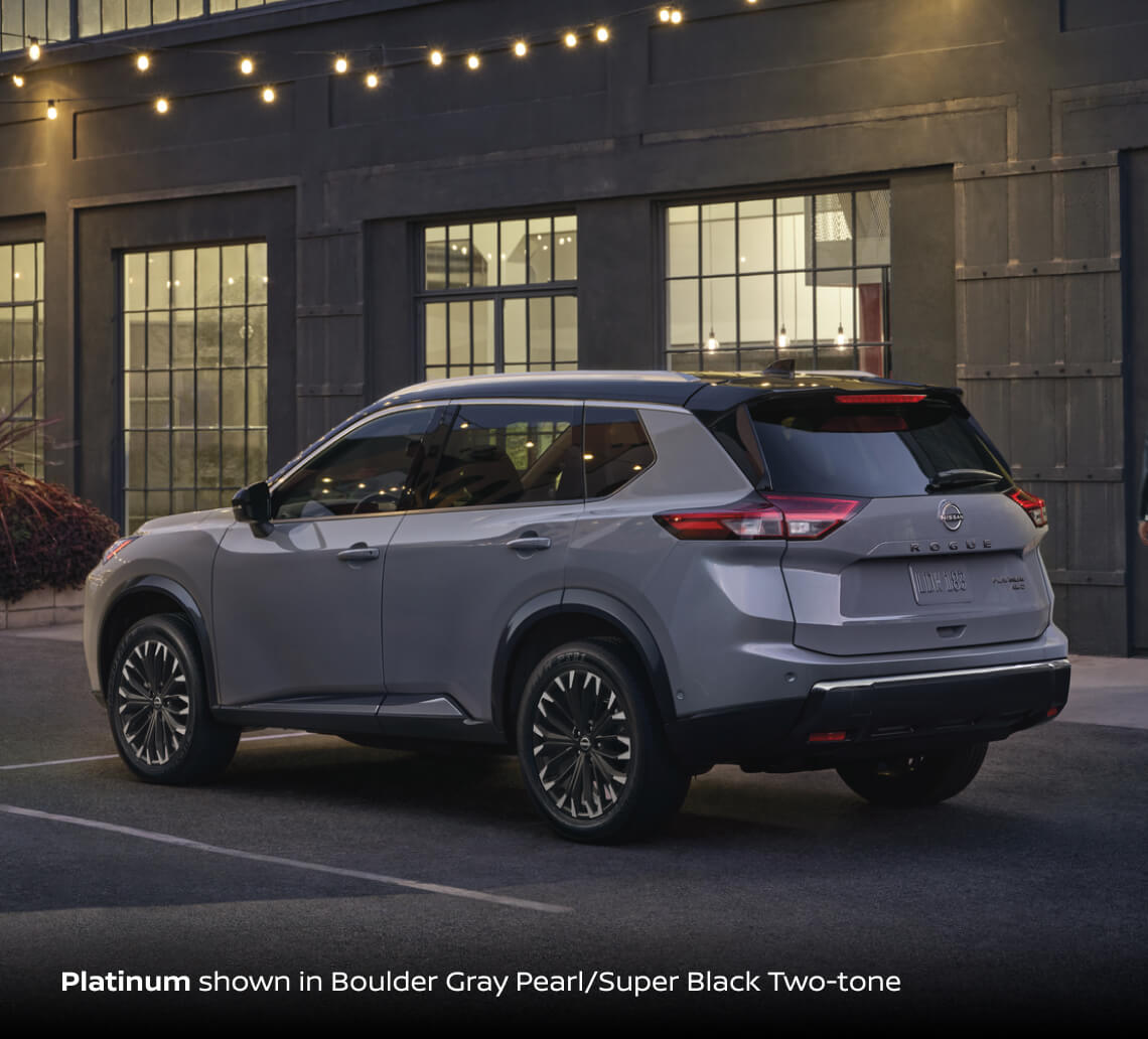 2026 Nissan Rogue Platinum AWD in Boulder Gray Pearl with Super Black roof, rear three-quarter view on city street at dusk.
